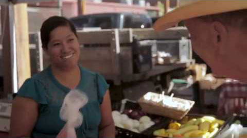 A woman in a fruit stand smiling and talking with a customer